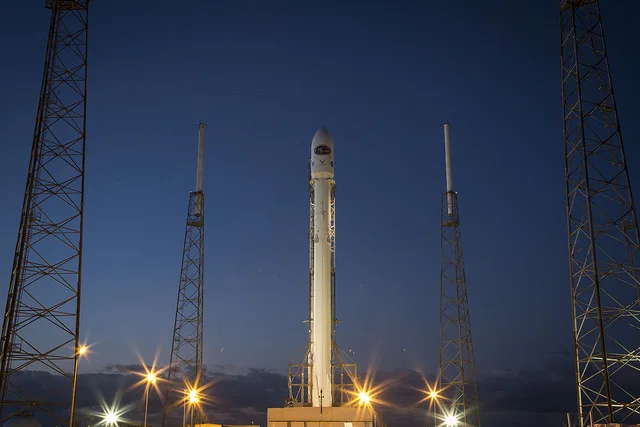 Rocket launch photograph with a small bright glare on the far-left tower above the lower lamps